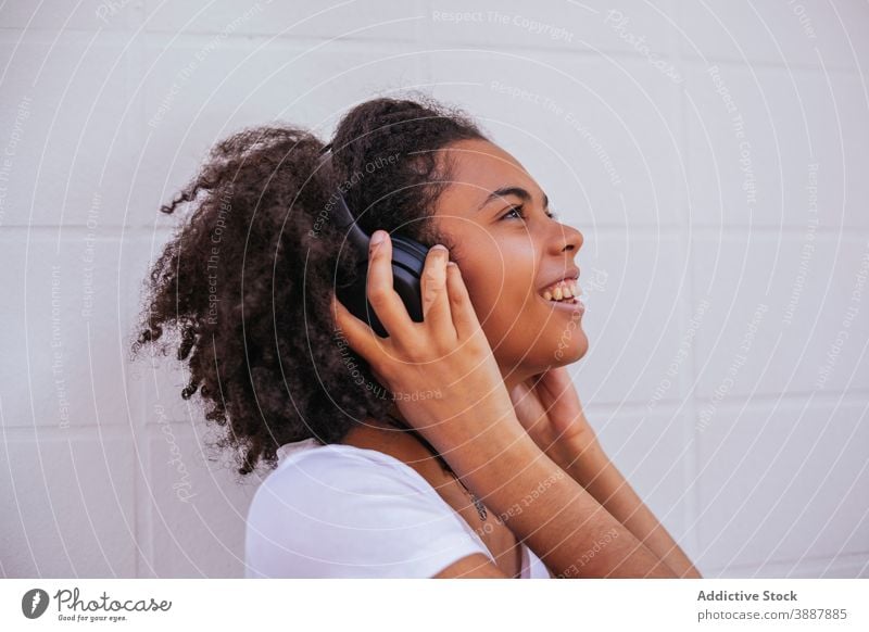 Delighted young woman listening to music in headphones song enjoy wireless street satisfied sound female ethnic black african american cheerful gadget glad tune
