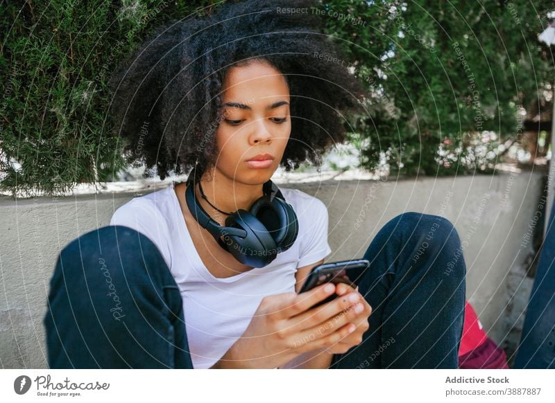 Young ethnic woman taking selfie in city headphones street self portrait urban afro hairstyle entertain unemotional female black african american building