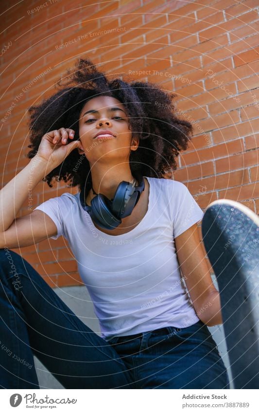 Delighted black woman with skateboard on street urban city weekend headphones cheerful young afro hairstyle female ethnic african american curly hair optimist