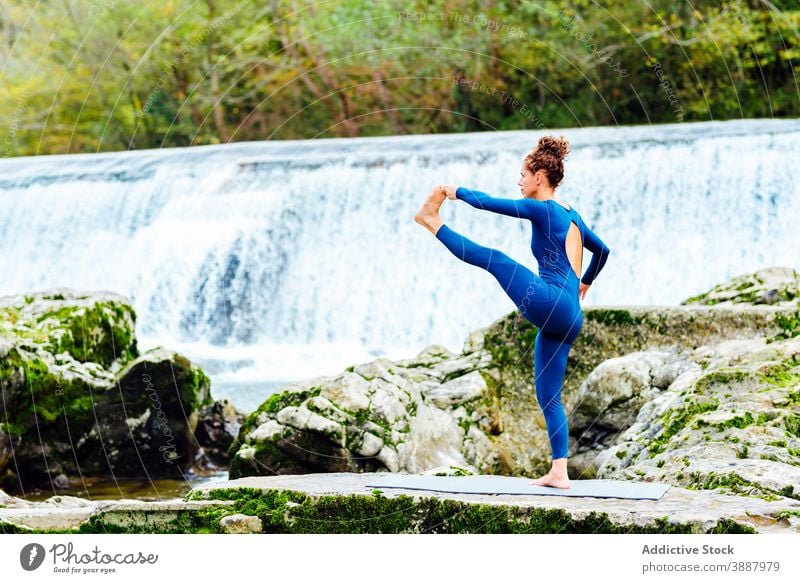 Woman doing yoga in Standing Hand to Toe pose in nature hand to toe pose woman flexible asana practice waterfall balance hasta padangusthasana female mat