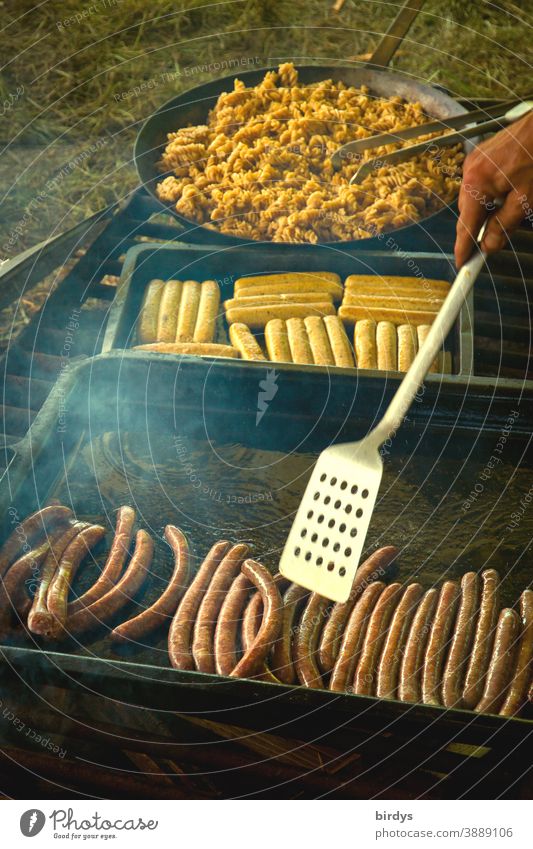 Grilling, frying, cooking on an open fire. Fried sausages, vegetarian sausages and noodle pan on large grill. BBQ boil Frying Bratwursts Noodles Smoke Hand