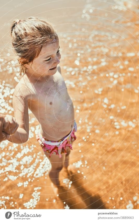 Close up of happy little girl standing in the sea looking away holding parent hand above recreation cute outdoors positive sunlight summertime splash family