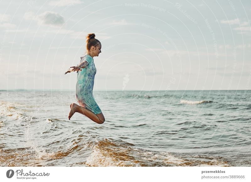 Girl enjoying sea jumping over waves spending a free time over sea on a beach during summer vacation excited positive sunset emotion carefree nature outdoors