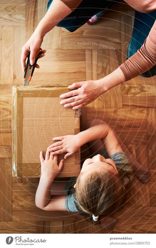 Woman unpacking a cardboard box parcel with help of her daughter view floor gift unboxing tape girl woman filler foam top open home wrapping opening shipping