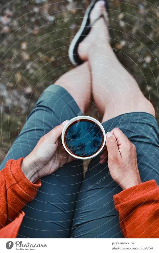 Close up of woman sitting outdoors holding cup with coffee above hiker wanderer trip wanderlust exploration lifestyle picnic camp freedom vacation travel