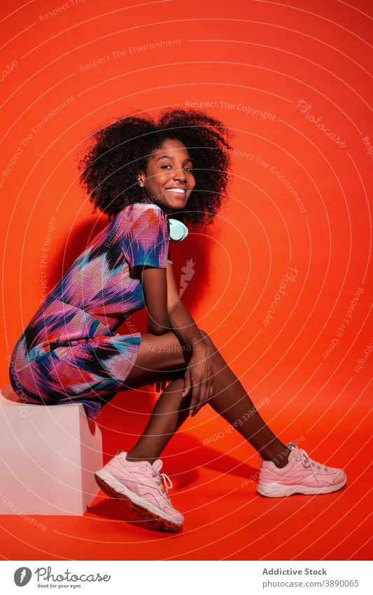 Young ethnic model in dress and sneakers vivid trendy woman millennial studio headphones afro hairstyle posture black african american cuban toothy smile
