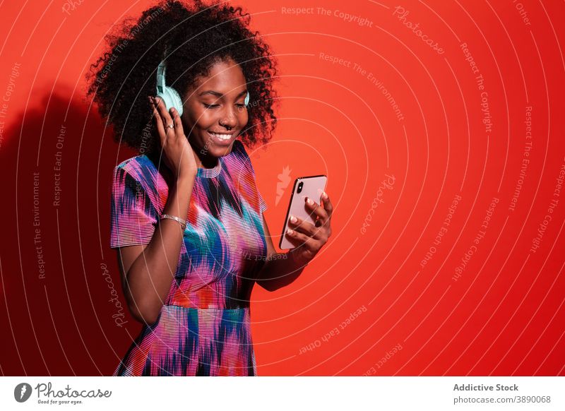 Cheerful black woman using smartphone and headphones music model bright style modern millennial selfie studio gadget listen vivid content casual social media