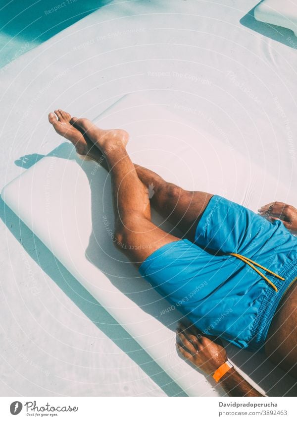 Crop man resting on lounger at poolside suntan deckchair sunbath vacation summer tourist relax lying traveler resort carefree hotel journey chill swimwear