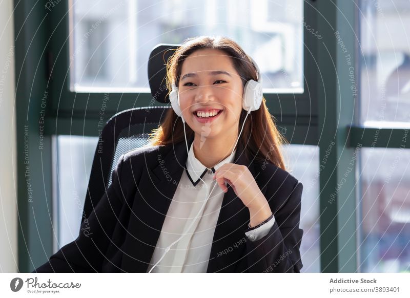 Cheerful ethnic woman with headphones working in office happy laugh communicate formal online device cheerful young asian female employee conversation modern
