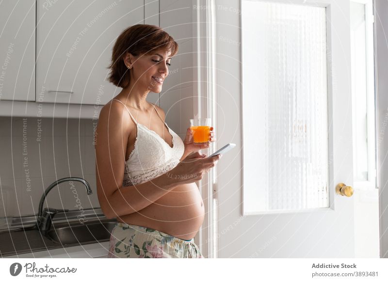 Delicate pregnant woman using smartphone in kitchen browsing home pregnancy tender message smile female gadget device prenatal surfing motherhood internet