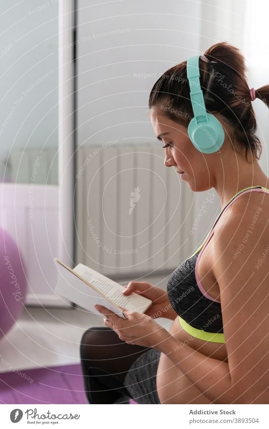 Pregnant woman stretching body and reading book during yoga practice pregnant listen music multitask pregnancy female activewear expect prenatal home healthy