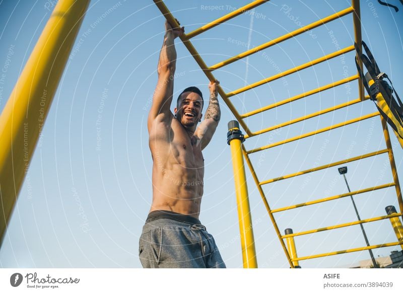 Athletic young man hanging from the bars at the calisthenics gym outdoors sport athlete muscles strength happy funny smile gymnastics street freestyle body