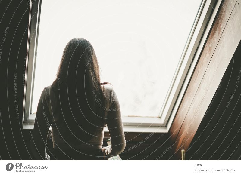 Rear view of a woman with long dark hair looking out of a window in a pitched roof Woman Window Pitch of the roof Skylight look out Back long hairs from behind