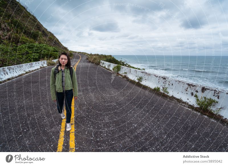 Woman with backpack walking on road on seashore traveler coast rocky woman ocean stormy adventure female active hiker backpacker nature direction route roadway