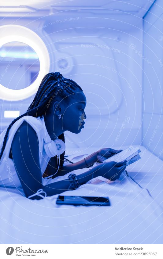 Young black woman reading brochure in capsule hotel bed rest traveler accommodation relax young female african american ethnic lifestyle tourism chill modern