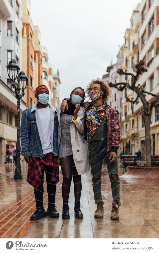 Trendy hipster friends in masks standing on city street coronavirus together cheerful urban modern group relationship positive friendship hug embrace pandemic