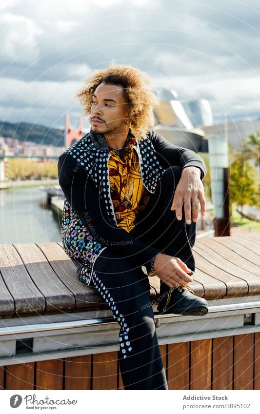 Confident trendy hipster man resting on street style informal fashion curly hair beard young modern colorful outfit guy african american black ethnic male