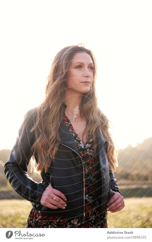 Serene woman standing in field at sunset style carefree serene leather jacket outfit nature enjoy female tranquil meadow sundown appearance long hair wavy hair