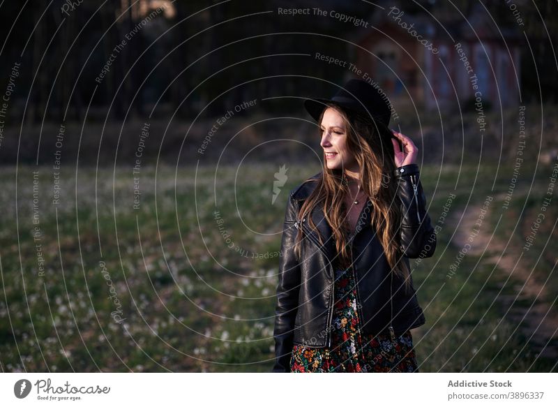 Charming woman in hat and leather jacket in countryside style sunset trendy outfit charming field female black apparel braid hairstyle long hair appearance
