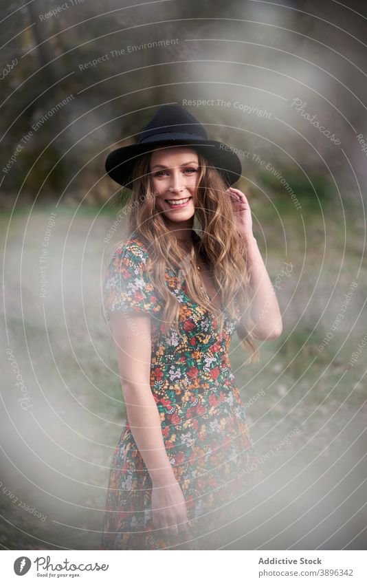 Glad woman in hat standing in forest accessory charming dress smile outfit nature apparel female woods appearance long hair wavy hair optimist style positive