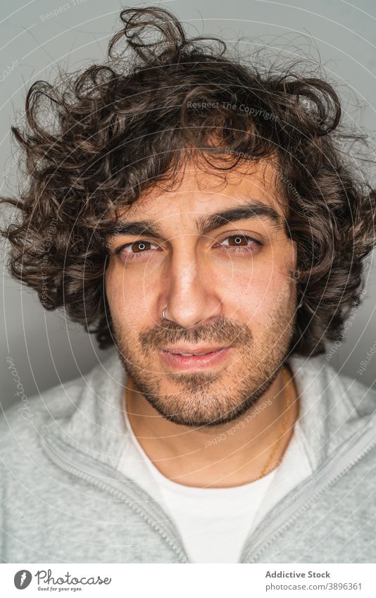 Serious young curly haired man looking at camera beard unshaven serious portrait casual handsome brunet ethnic hispanic hipster modern tired male confident