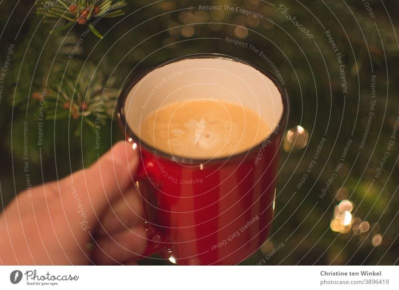 Advent coffee. Hand holding red cup with cappuccino. Close-up with fir green and some shiny blurred lights in the background Coffee mug Cappuccino To hold on