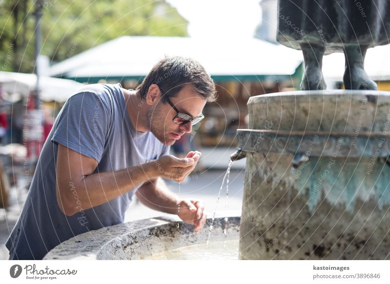 Thirsty young casual cucasian man drinking water from public city fountain on a hot summer day hydrate thirsty hydration outdoors refreshing park wet spout