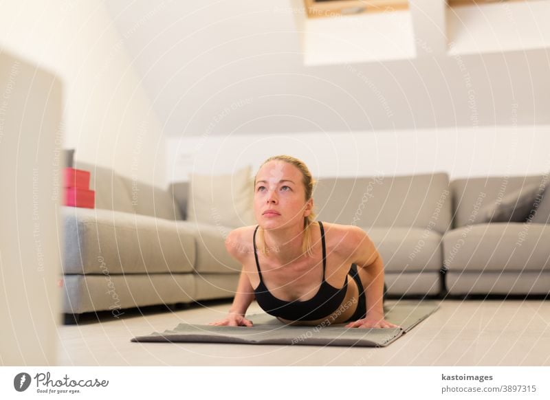 Beautiful blonde woman doing home workout indoors. Woman practice yoga at home. Fit girl using workout tutorials for healthy active lifestyle. Woman using quarantine for home workouts.