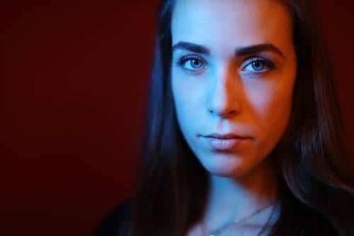 Portrait of a young woman in a room in front of a red wall with red and blue light Student daintily Facial expression empathy Looking into the camera