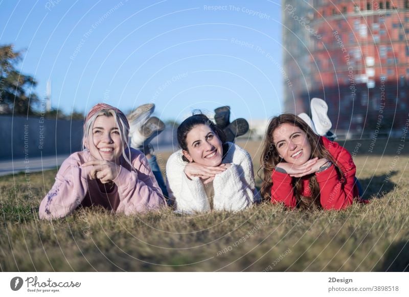 Three beautiful young women lie on the lawn, resting and daydreaming in the park on the green grass. happy lying woman three smiling friendship ground female