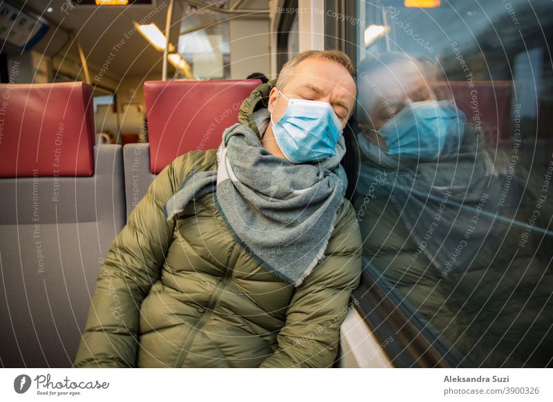 Traveling in public transport during the pandemic. Tired middle aged man wearing medical protective mask on his face sleeping in commuter train. city