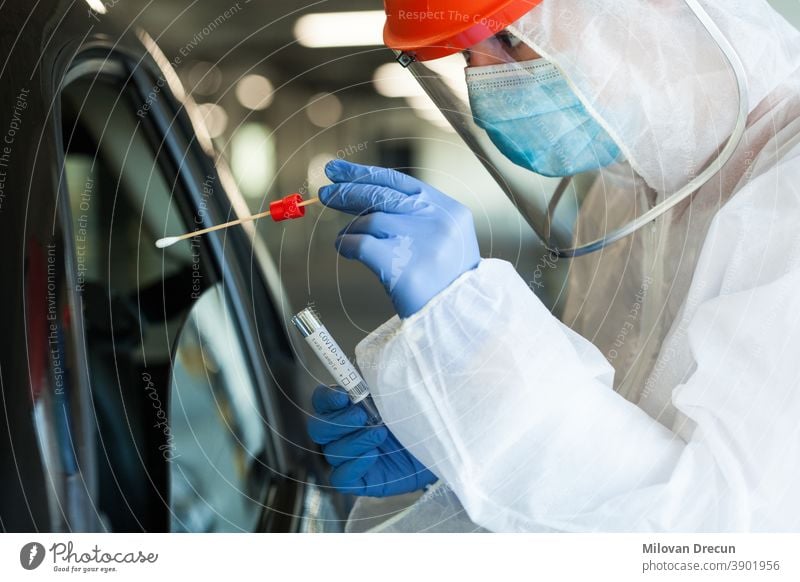 Medical NHS worker in personal protective equipment swabbing a person in a car drive through Coronavirus COVID-19 mobile testing center,oral and nasal specimen collection procedure,health and safety