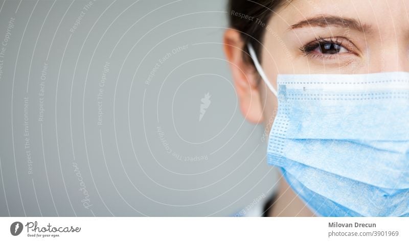 Close up of female UK NHS EMS doctor's face,wearing blue PPE surgical protective mask,COVID-19 Coronavirus disease,global pandemic outbreak,deadly SARS-CoV-2 epidemic,copy space on left side of frame