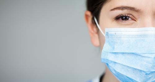 Close up of female UK NHS EMS doctor's face,wearing blue PPE surgical protective mask,COVID-19 Coronavirus disease,global pandemic outbreak,deadly SARS-CoV-2 epidemic,copy space on left side of frame