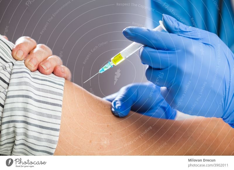 Coronavirus COVID-19 immunisation concept,medical worker wearing blue protective latex gloves holding syringe filled with yellow liquid,giving patient vaccine shot dose,caucasian hand closeup detail