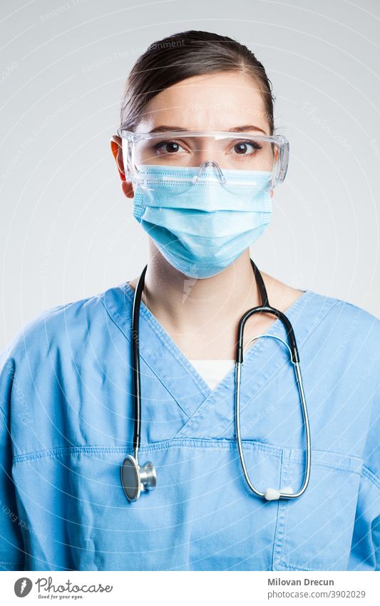 Young serious female EMS UK key worker doctor,portrait isolated on white background in ICU facility,wearing PPE Personal Protective Equipment,face mask,safety goggles,COVID-19 pandemic outbreak crisis