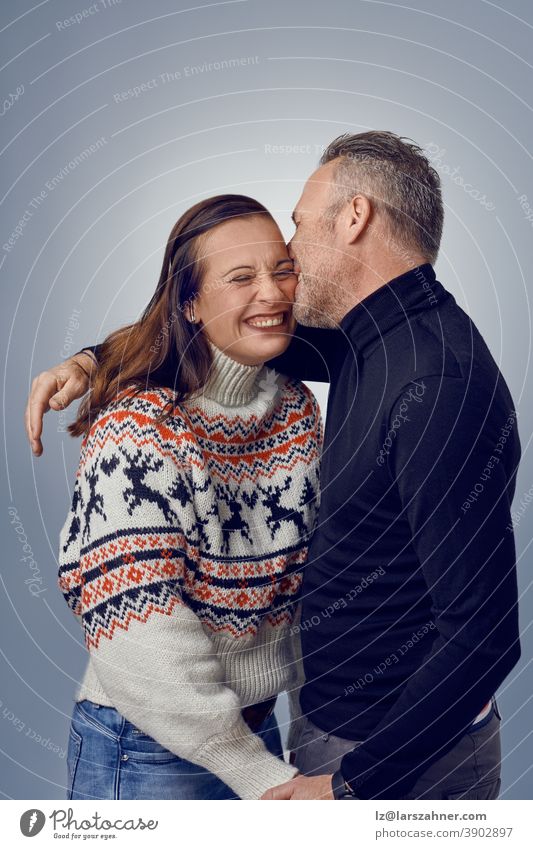 Adult man kissing his happy laughing wife. Loving couple in warm sweaters posing for family portrait. Winter holidays photoshoot concept in studio woman married