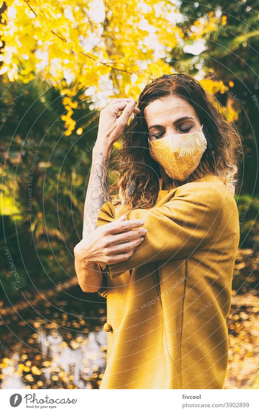 woman with mask in a park II retouching hair yellow garden yellowish leafs lifestyle mature portrait one people tree coat yellow overcoat scene romantic