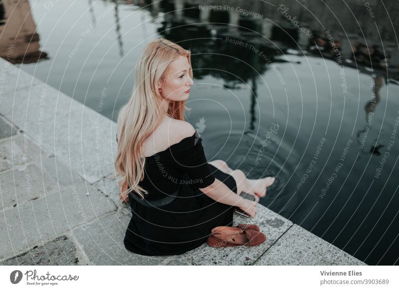 Woman Sitting by The Water With Bare Feet blonde long hair woman elegant black dress meditation relaxing nature water lake river bathing bathe thinking