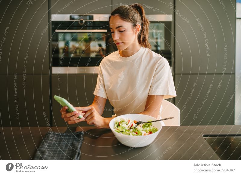 Woman having lunch and browsing smartphone at home woman eat salad vegetable healthy food kitchen social media female read news internet online surfing watch