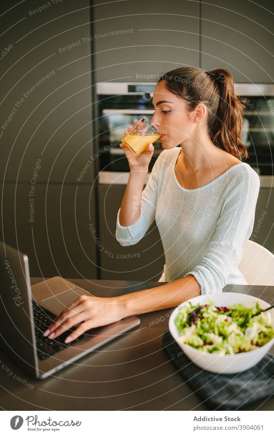 Woman drinking juice and working on laptop in kitchen woman freelance orange lunch home remote entrepreneur female project beverage fresh refreshment gadget