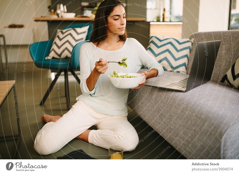 Young woman eating salad and watching video on laptop at home healthy young gadget food female casual lifestyle internet online using meal connection rest