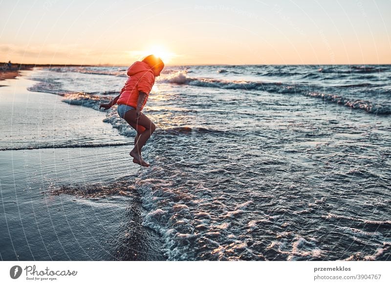 Playful little girl jumping over sea waves on a sand beach at sunset excited free enjoy positive emotion carefree nature outdoors travel happiness happy summer