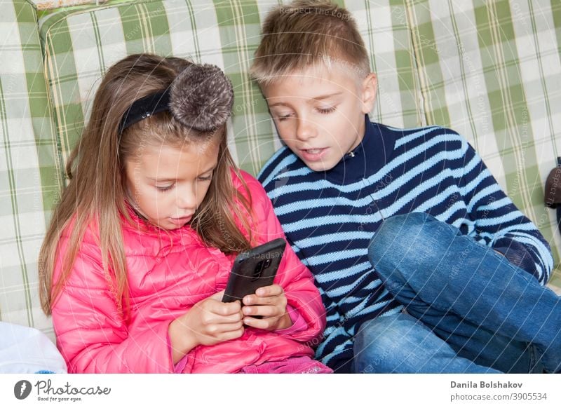 Girl is sitting on swing and playing mobile games on smart phone. boy sits next to her and worries about process of playing friend. Image with selective focus