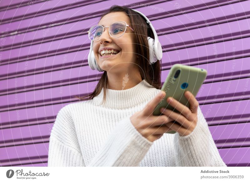 Cheerful woman talking on phone near wall of building millennial smartphone speak city street urban using female device gadget call mobile phone glad smile