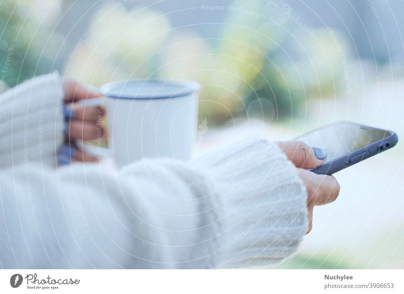 Close up woman hands holding hot cup of coffee or tea and using smartphone in cold weather background, wearing warm fur knitted clothes beautiful chocolate