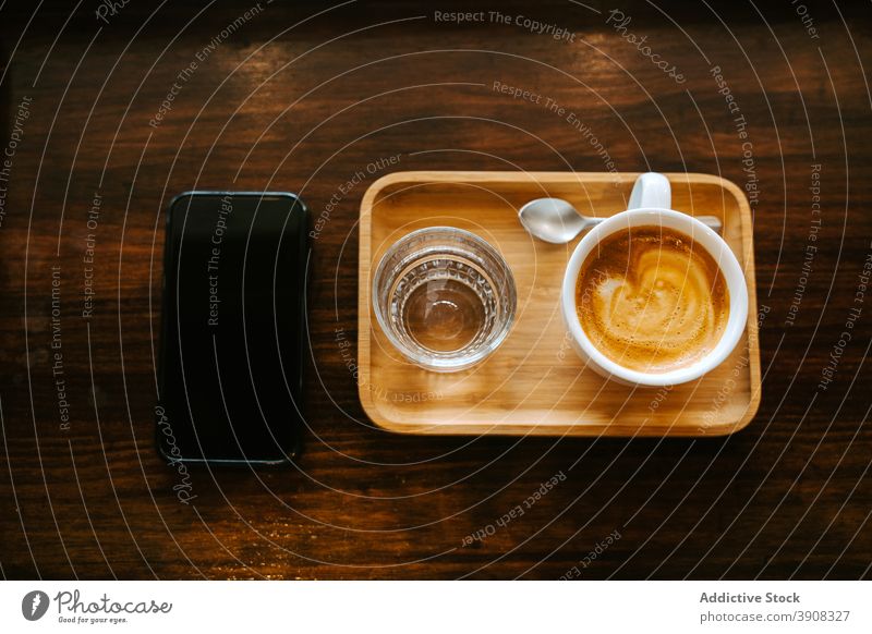 Cup of coffee and glass of water placed near smartphone cup mobile drink serve cafe gadget wooden table cappuccino device beverage morning lifestyle cellphone