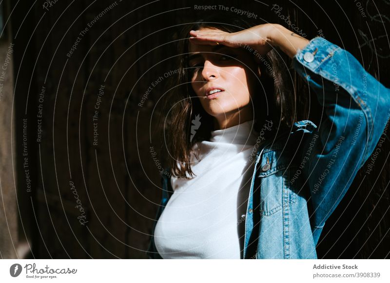 Young woman protecting eyes from sun sunlight cover eyes brunette confident young female denim jacket sunshine shadow gesture ethnic shade black millennial