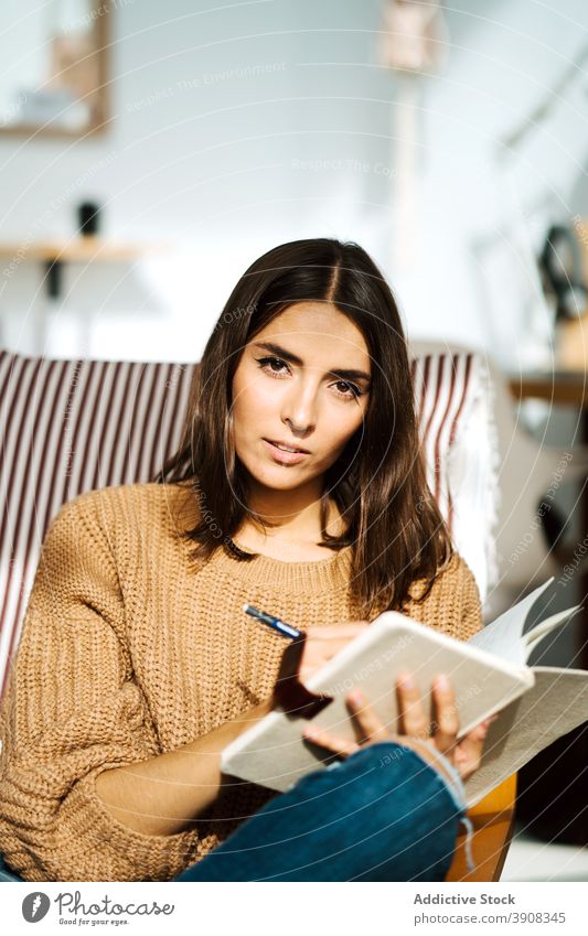 Cheerful woman taking notes in notebook take note write diary smile weekend enjoy home notepad female outfit armchair casual sit relax modern young cozy