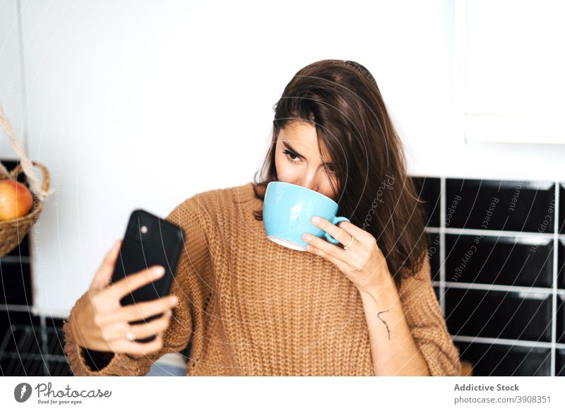 Woman drinking coffee taking selfie with smartphone woman browsing home self portrait kitchen relax cup weekend photo domestic picture female counter mobile